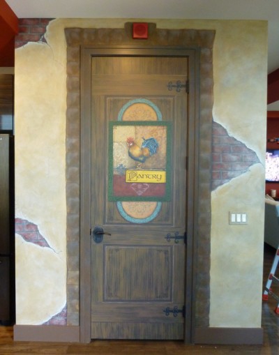 Pantry Door painted to look like old wood with old wrought iron hardware, beautiful signage with a rooster. Walls painted to look like old stucco, cracked and broken away to reveal bricks. Stone surround on the doorframe. Mural by Ellen Leigh